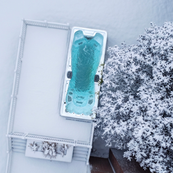 A drone view of a swim spa running in winter surrounded by snow.