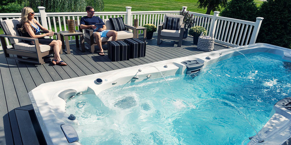 A couple relaxing on their deck next to a swim spa with the water features on.