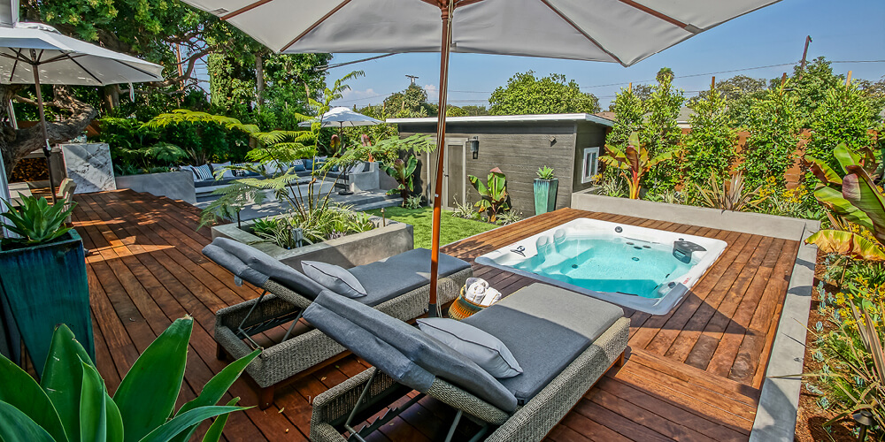 H2X Therapool D swim spa on a back patio with lounge chairs and a sun umbrella.